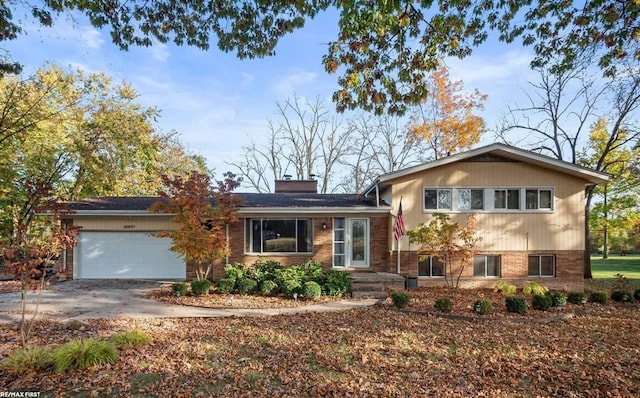 split level home featuring brick siding, driveway, a chimney, and a garage