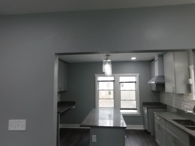 kitchen featuring a sink, backsplash, wall chimney range hood, baseboards, and dark wood-style flooring