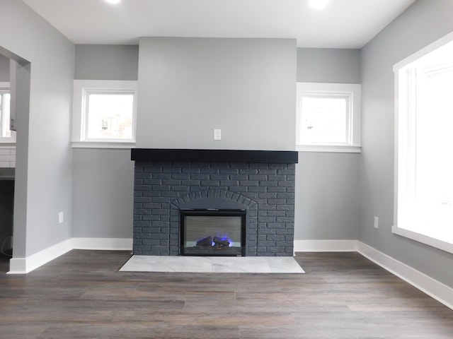 unfurnished living room with a brick fireplace, baseboards, and wood finished floors