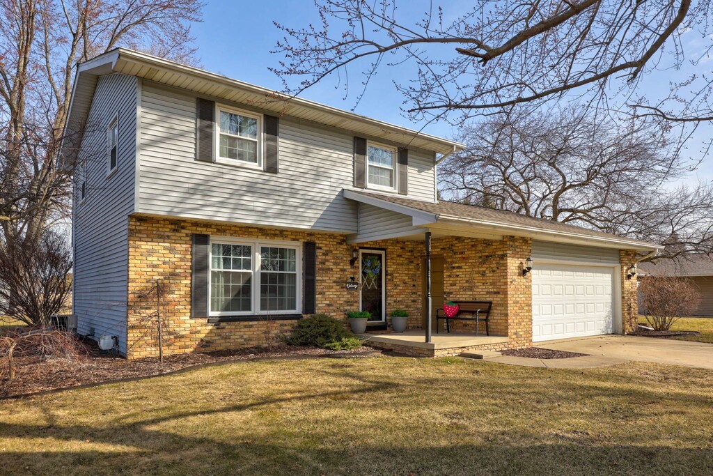 view of front of house with brick siding, a front yard, an attached garage, and driveway