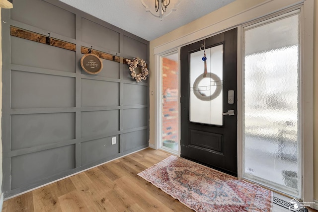 foyer with a wealth of natural light, a decorative wall, a textured ceiling, and wood finished floors