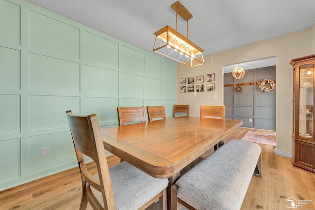 dining room with a textured ceiling, light wood-style floors, and a decorative wall