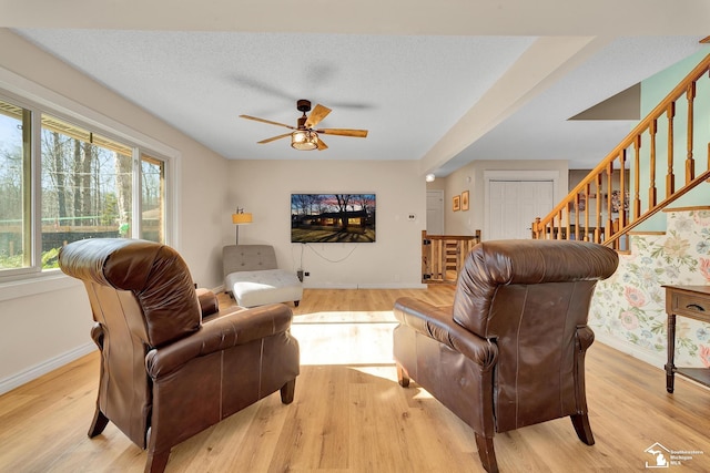 living area with a textured ceiling, stairs, light wood-type flooring, and baseboards