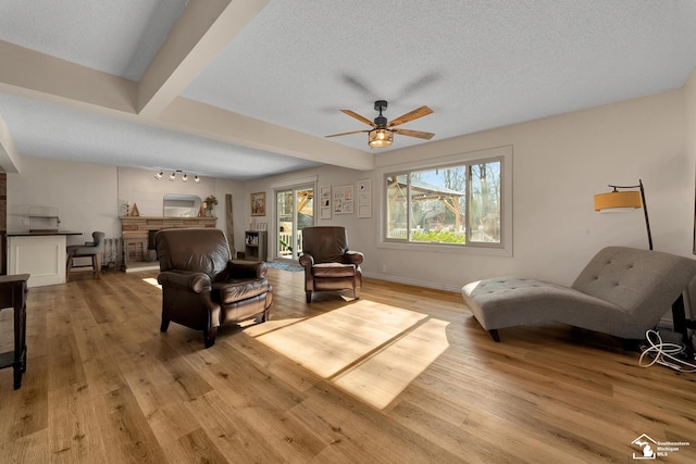 living area with light wood-style flooring, a textured ceiling, baseboards, and a ceiling fan