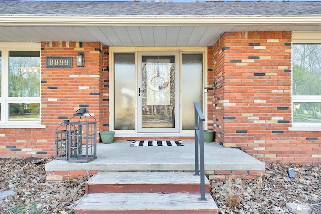 entrance to property featuring covered porch, brick siding, and a shingled roof