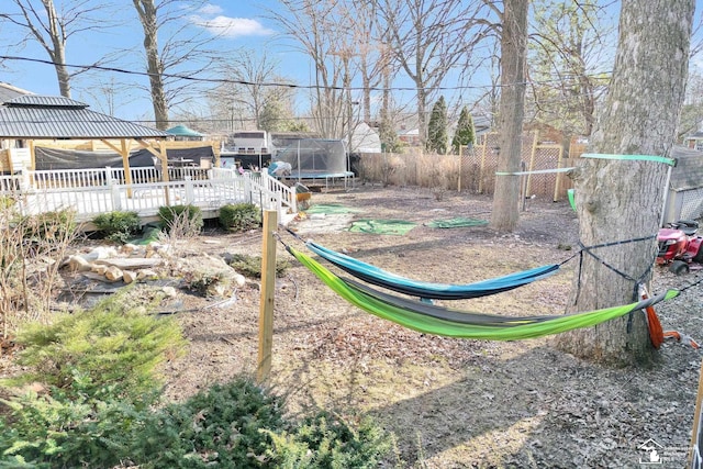 view of yard featuring a wooden deck, a trampoline, and fence