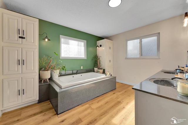 full bathroom with a textured ceiling, a bath, wood finished floors, and a sink