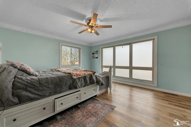 bedroom featuring a ceiling fan, baseboards, visible vents, light wood finished floors, and a textured ceiling