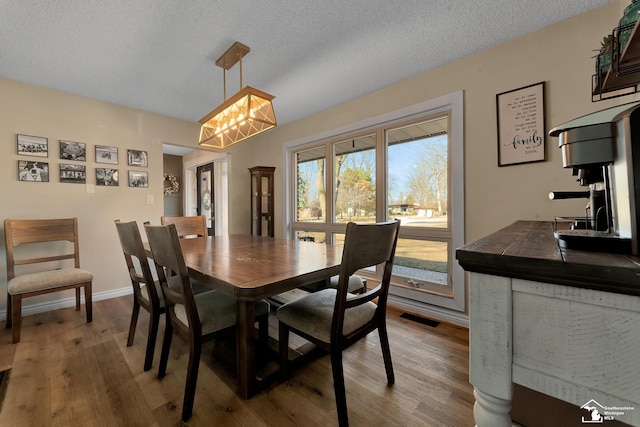 dining room featuring visible vents, baseboards, a textured ceiling, and wood finished floors