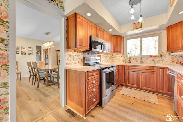 kitchen featuring decorative backsplash, stainless steel appliances, light wood-type flooring, and light countertops