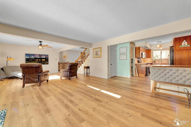 living room featuring light wood finished floors, baseboards, stairs, a textured ceiling, and a ceiling fan