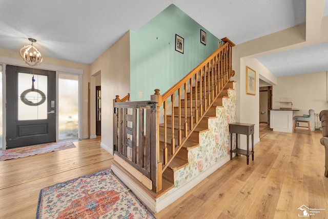 entrance foyer featuring an inviting chandelier, stairway, baseboards, and wood-type flooring