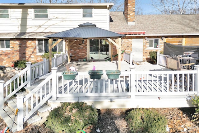 back of house with a gazebo, brick siding, roof with shingles, and a chimney