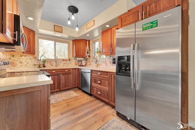 kitchen with light wood finished floors, stainless steel appliances, light countertops, a raised ceiling, and brown cabinets