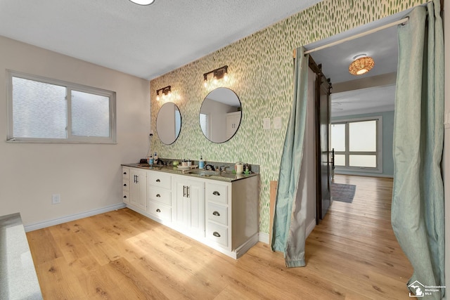 bathroom with wood finished floors, wallpapered walls, baseboards, and a sink