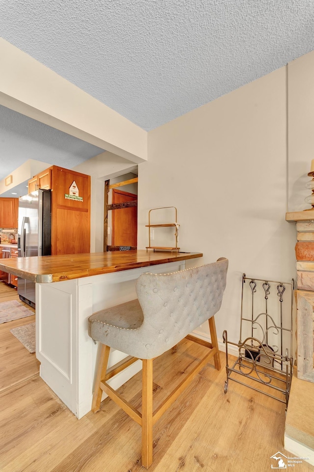 bar featuring light wood-style floors, stainless steel refrigerator with ice dispenser, and a textured ceiling