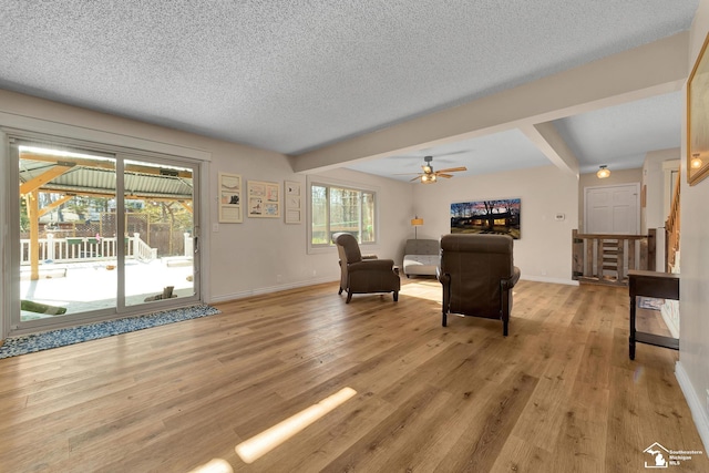 living area featuring beamed ceiling, light wood-style floors, baseboards, and a textured ceiling