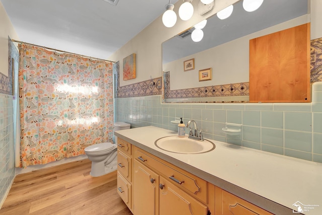 bathroom with a wainscoted wall, toilet, wood finished floors, tile walls, and vanity