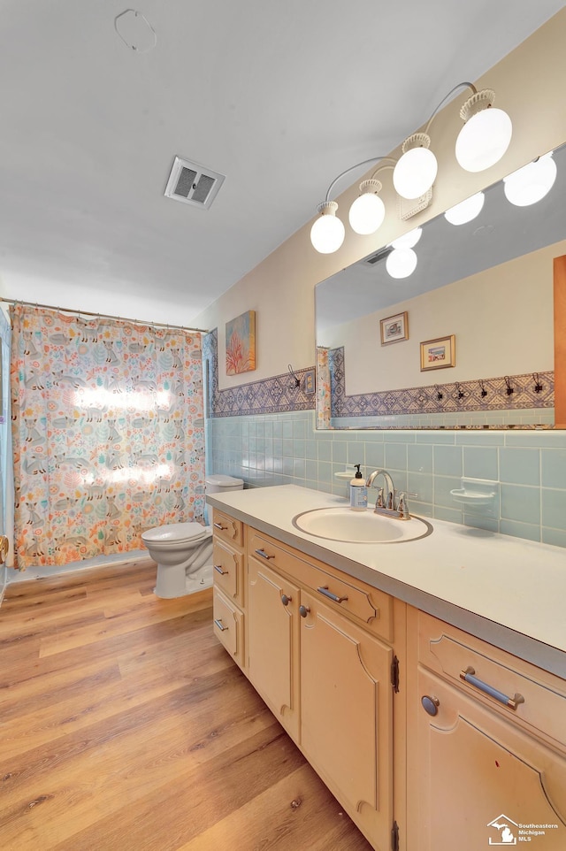 full bathroom with visible vents, toilet, wood finished floors, tile walls, and vanity