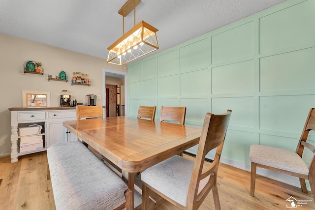 dining space with a decorative wall, light wood-style floors, and a textured ceiling