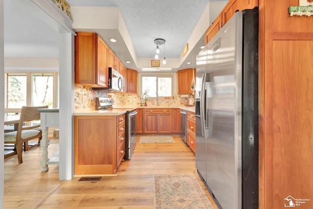 kitchen featuring stainless steel appliances, light wood-style flooring, decorative backsplash, and light countertops