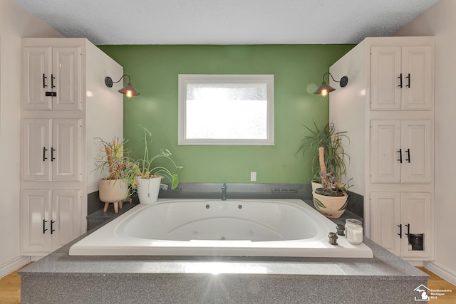 bathroom with a textured ceiling, wood finished floors, and a whirlpool tub