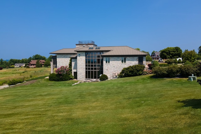 rear view of property with metal roof, stone siding, a lawn, and a standing seam roof