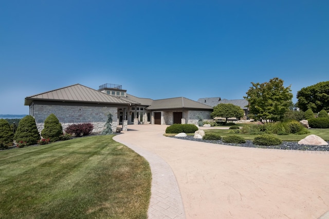 view of front of house with a front yard, driveway, a standing seam roof, stone siding, and metal roof
