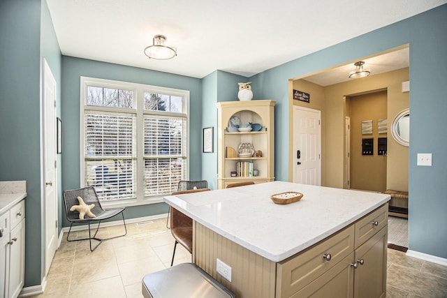 kitchen with light tile patterned floors, baseboards, a center island, and light stone countertops