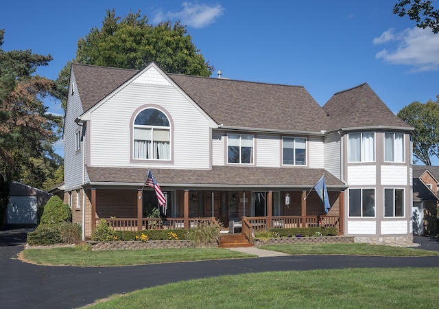 view of front facade featuring a front yard, roof with shingles, covered porch, and brick siding