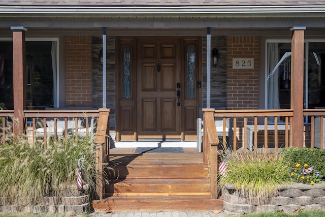 property entrance with a porch, brick siding, and a shingled roof