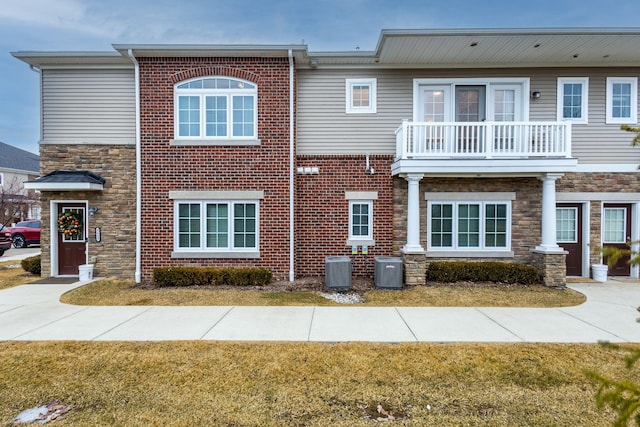 view of front of home with cooling unit, a front yard, brick siding, and a balcony