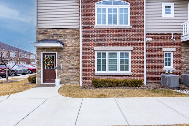 doorway to property with central air condition unit, stone siding, and brick siding