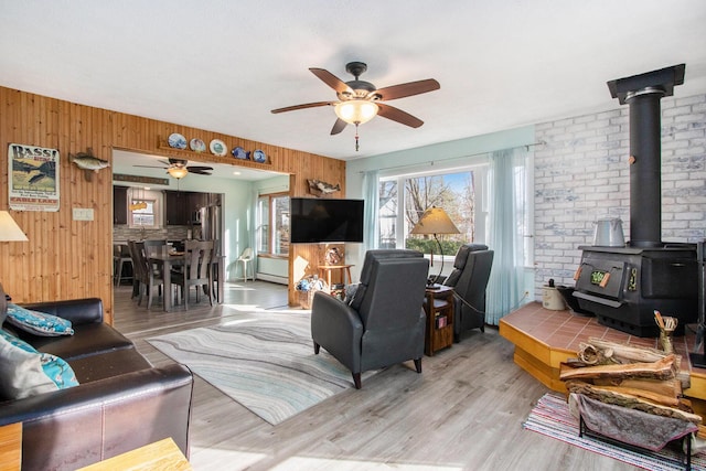 living room featuring wooden walls, light wood-type flooring, a wood stove, and a ceiling fan