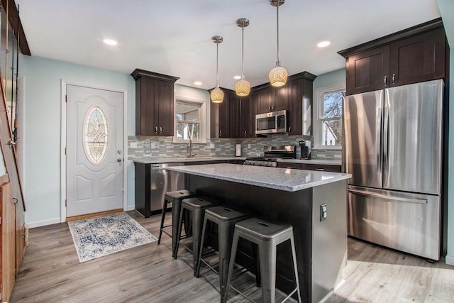 kitchen featuring light stone counters, light wood finished floors, stainless steel appliances, decorative backsplash, and dark brown cabinetry