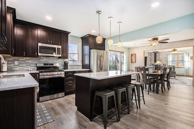 kitchen featuring light wood-type flooring, a sink, a kitchen breakfast bar, dark brown cabinetry, and appliances with stainless steel finishes