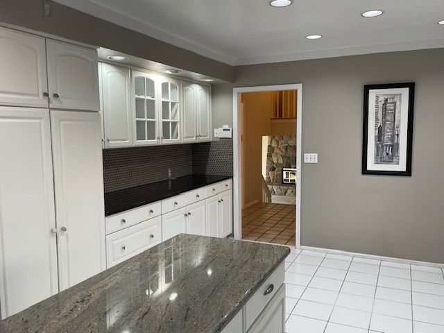 kitchen with dark stone countertops, light tile patterned floors, white cabinets, glass insert cabinets, and tasteful backsplash