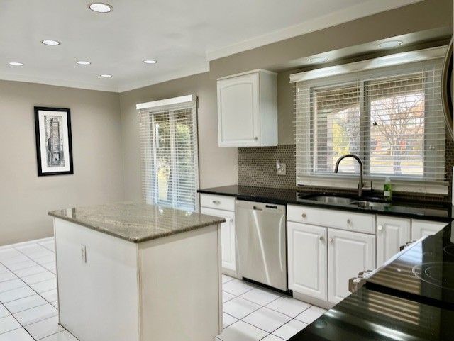 kitchen with a kitchen island, dishwasher, ornamental molding, white cabinetry, and a sink