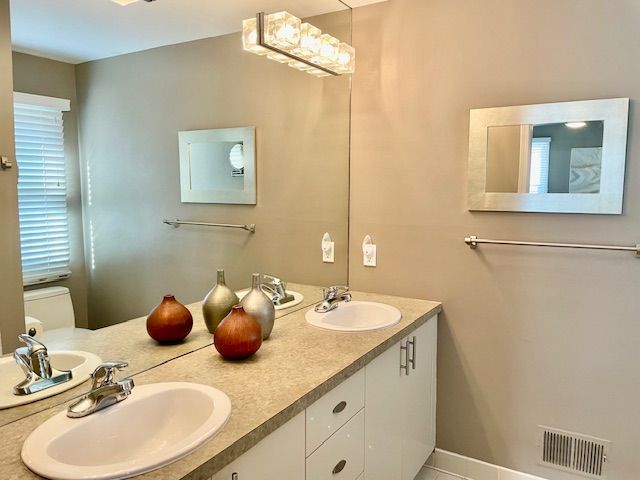 bathroom with double vanity, toilet, visible vents, and a sink