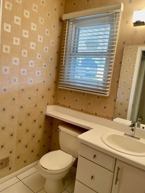 bathroom featuring vanity, baseboards, wallpapered walls, tile patterned floors, and toilet