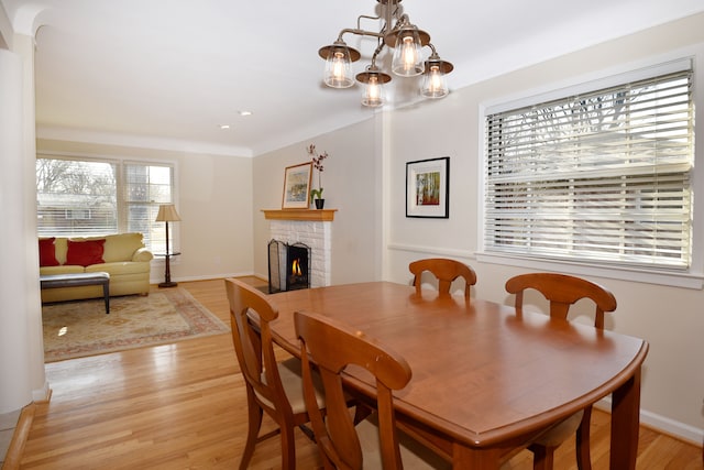 dining room featuring a chandelier, a brick fireplace, baseboards, and light wood-style floors