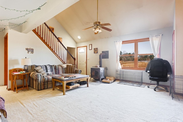 carpeted living room featuring stairs, high vaulted ceiling, a ceiling fan, and a wood stove