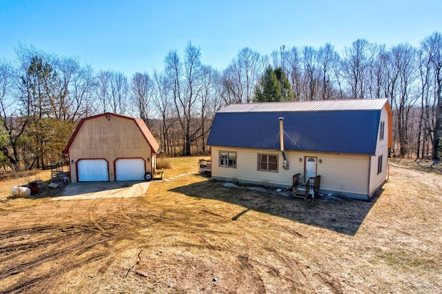 exterior space with a gambrel roof, driveway, metal roof, an outdoor structure, and a garage