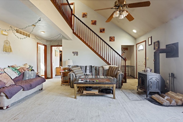 carpeted living area featuring a wood stove, high vaulted ceiling, stairs, and a ceiling fan