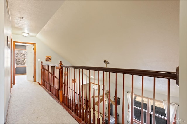 hall featuring lofted ceiling, carpet flooring, an upstairs landing, and a textured ceiling