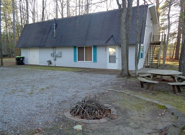 rear view of property with stairs, a gambrel roof, roof with shingles, and dirt driveway