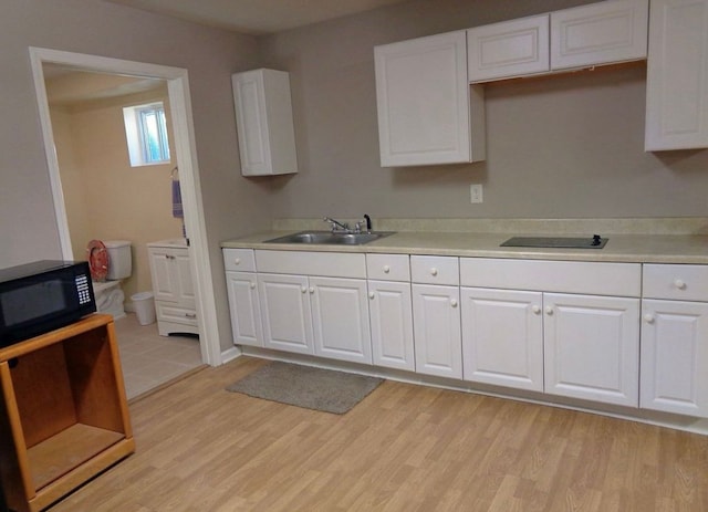 kitchen featuring light wood finished floors, black appliances, light countertops, and a sink