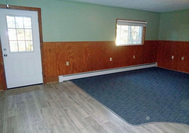 unfurnished room featuring baseboard heating, wainscoting, wooden walls, and wood finished floors