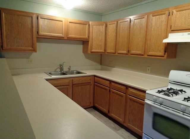 kitchen featuring a sink, under cabinet range hood, gas range gas stove, a textured ceiling, and light countertops