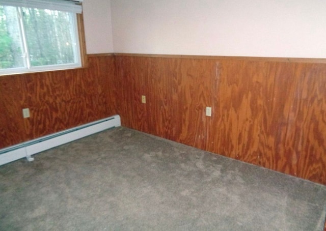 empty room featuring baseboard heating, carpet, wood walls, and wainscoting